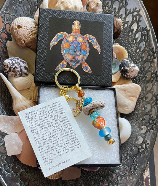 Decorative keychain with beads and a turtle charm in a box, surrounded by seashells.