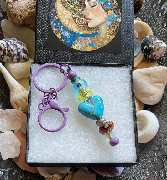 Colorful beaded keychain in a decorative box with seashells in the background