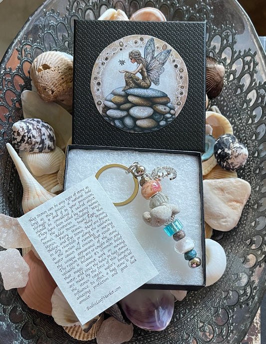Keychain with fairy design in a decorative box on a textured surface with shells.
